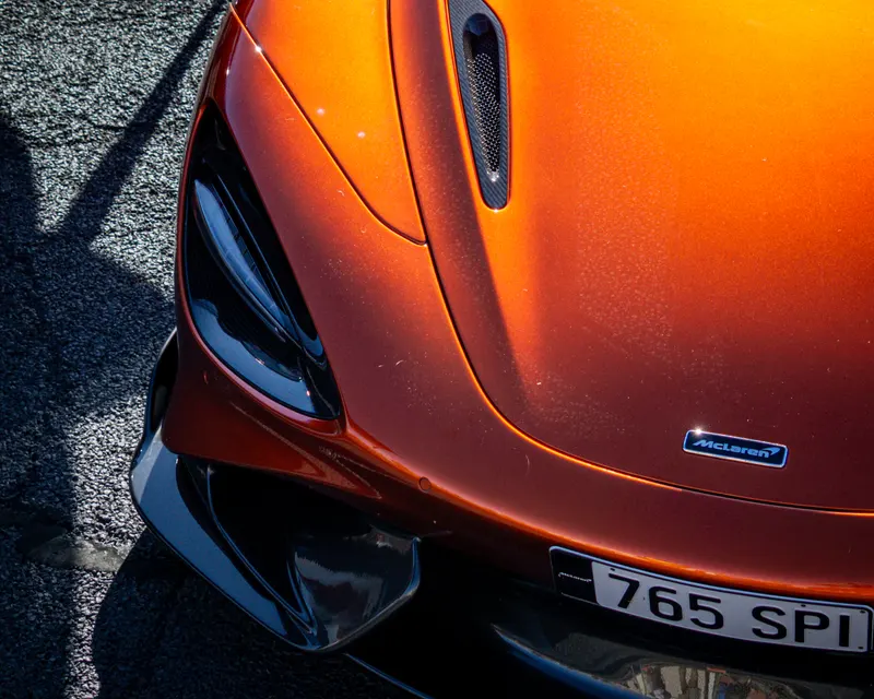 Overhead detail of an orange McLaren bonnet, badge and headlight