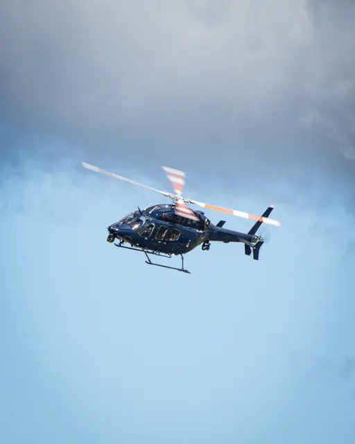 Helicopter flying through open blue sky beneath dark clouds