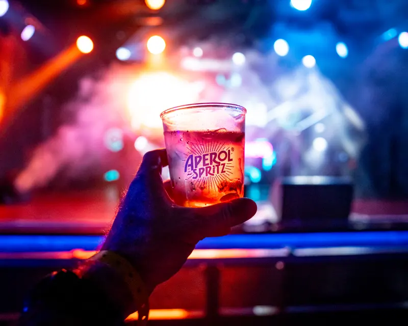 Aperol Spritz cup held against colourful stage lighting