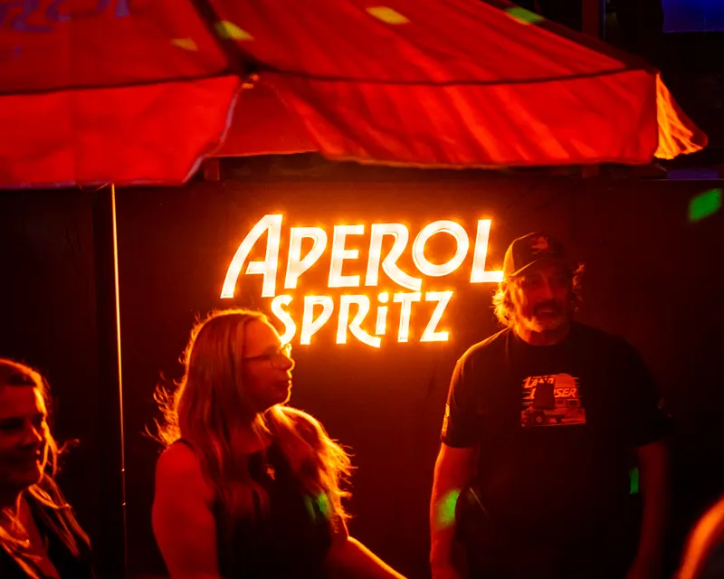 Guests beneath an illuminated Aperol Spritz sign
