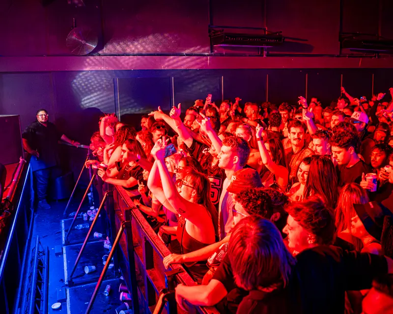 Crowd at the front barrier under red stage lighting