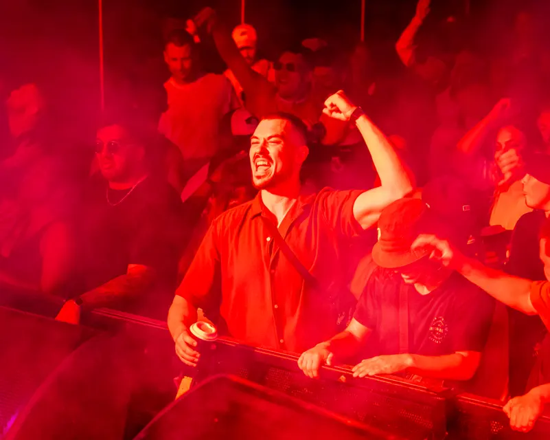 Guest cheering with an arm raised under red lighting