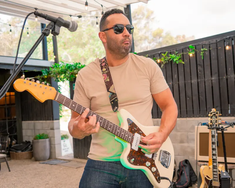 Guitarist performing outdoors with a white electric guitar