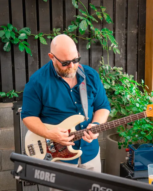 Bassist performing outdoors against a dark timber wall