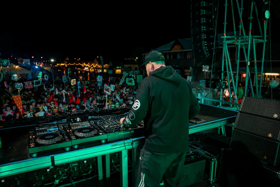 DJ viewed from behind on an outdoor stage facing a crowd