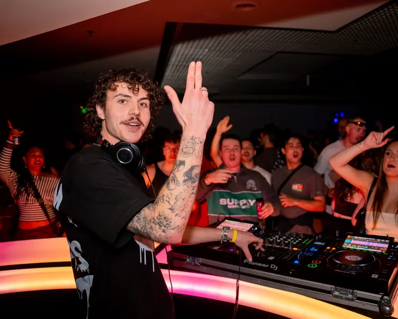 DJ gesturing to the crowd from behind the decks in a nightclub