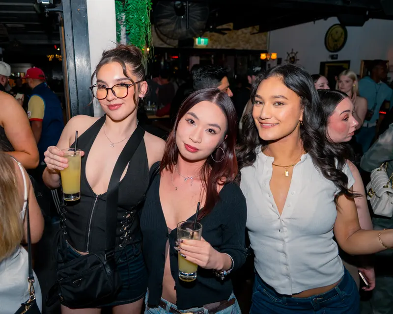 Three guests with drinks posing together at a bar